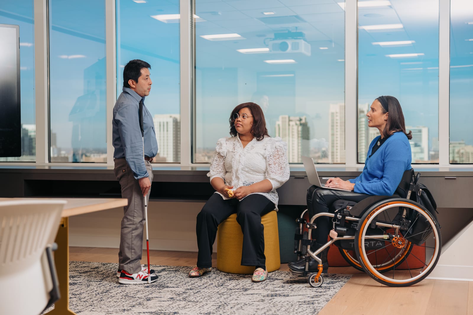 Three colleagues having an enthusiastic conversation in an accessible office environment.